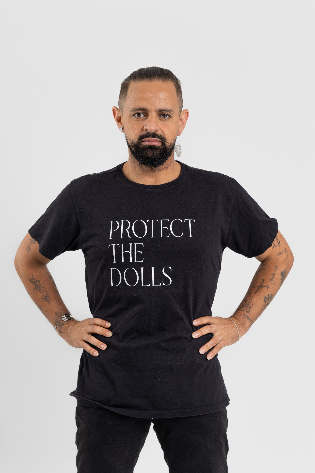 Jayslan Souza em pé, com as mãos na cintura, usando camiseta preta com a frase Protect the Dolls.